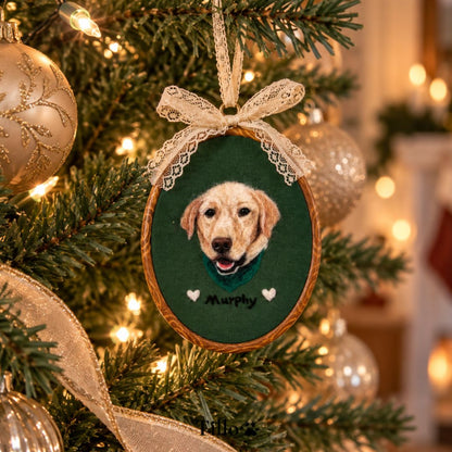 A personalized oval Christmas ornament featuring a painted golden retriever portrait named 'Murphy' on a dark green background, hanging on a decorated Christmas tree with warm lights and ornaments.